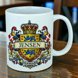 Introducing the Mug: Denmark Coat of Arms Custom Name Ceramic Mug (11 oz Capacity) by Nordic Wholesale—a striking white ceramic heritage mug. This personalized mug features a vibrant Danish coat of arms with your custom name in bold, two Danish flags, and “Danmark” elegantly displayed on a ribbon at the bottom. Iconic design elements include lions, hearts, and a crown for an authentic touch of Denmark’s heritage.