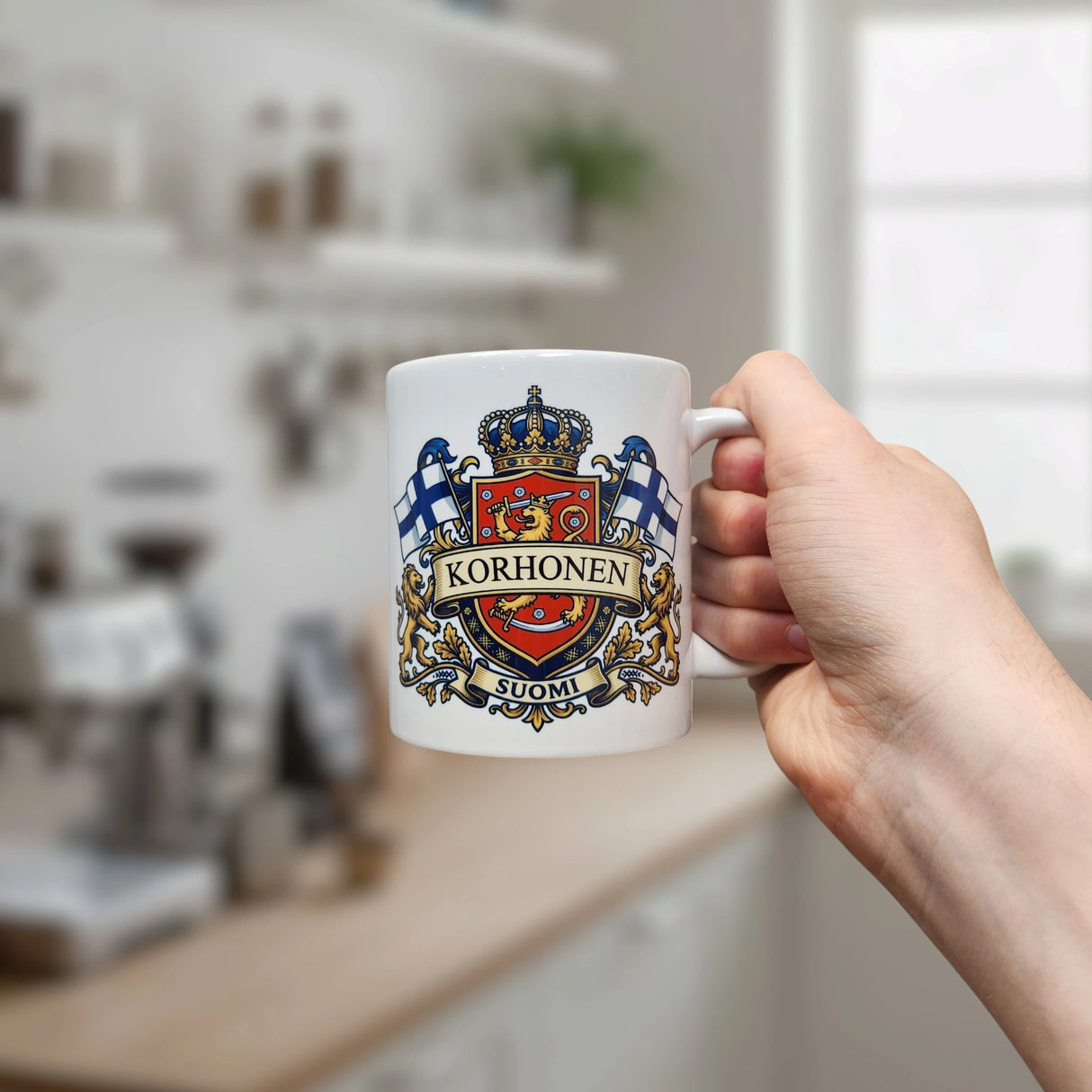 A hand displays the Nordic Wholesale Mug: Finland Coat of Arms Custom Name Ceramic Mug (11 oz Capacity), featuring a white finish with a detailed crest, two Finnish flags, and "Korhonen" above "Suomi" on the front. Set against a bright, contemporary kitchen backdrop with blurred shelves and a window, this mug is an ideal personalized family gift for anyone proud of their Finnish heritage.