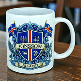 A Nordic Wholesale Mug: Iceland Coat of Arms Custom Name Ceramic Mug (11 oz Capacity), personalized with the name JÓNSSON, features a blue heraldic crest with Icelandic flags and mythical creatures above the word ÍSLAND, and is displayed on a wooden table.