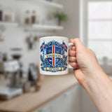 A hand holds the Nordic Wholesale Mug: Iceland Coat of Arms Custom Name Ceramic Mug (11 oz Capacity), featuring a white design personalized with the name Jonsson, an ornate blue crest, two Icelandic flags, and the word "Island." A blurred kitchen appears in the background.
