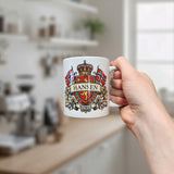 A hand holds the Mug: Norway Coat of Arms Custom Name Ceramic Mug (11 oz Capacity) by Nordic Wholesale, personalized with the Norwegian coat of arms, two Norwegian flags, and the words “Hansen” and “Norge.” A blurred kitchen with shelves and a window forms a cozy backdrop, highlighting this unique Norway heritage gift.