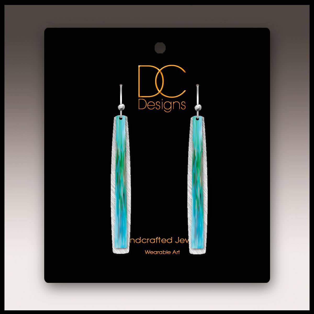 A pair of aqua abstract icicle multilayer handmade earrings on a black DC Designs card labeled Handcrafted Jewelry and Wearable Art.