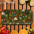 Birchwood tray featuring houses, crows, mushrooms, and leaves in a nature motif. The tray is surrounded by assorted fruits and vegetables on a wooden table.