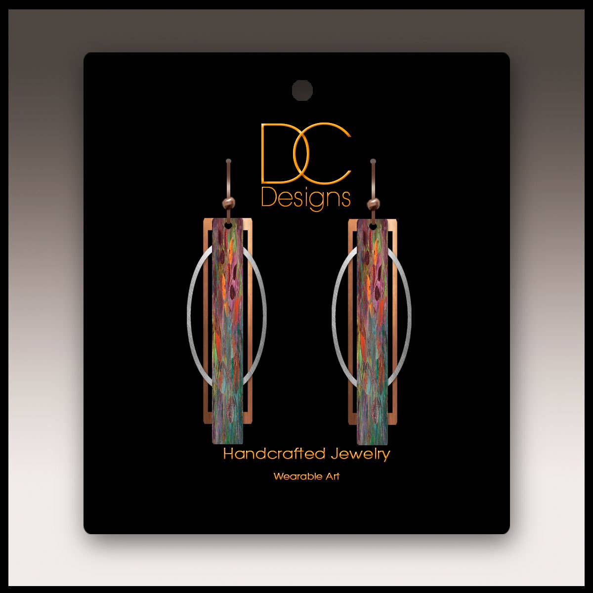 Handmade orange and green geometric multilayer earrings with metal accents and hypoallergenic stainless steel hooks, displayed on a black card labeled DC Designs Handcrafted Jewelry Wearable Art.
