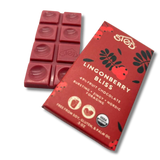 Red chocolate bar with lingonberry pieces next to a wrapper showing Nordic summer berries and icons indicating free from soy, gluten, and palm oil.