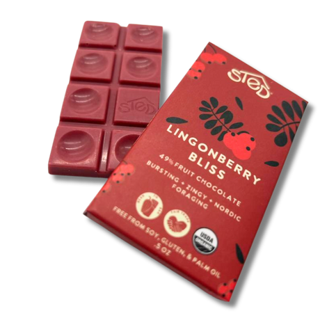 Red chocolate bar with lingonberry pieces next to a wrapper showing Nordic summer berries and icons indicating free from soy, gluten, and palm oil.