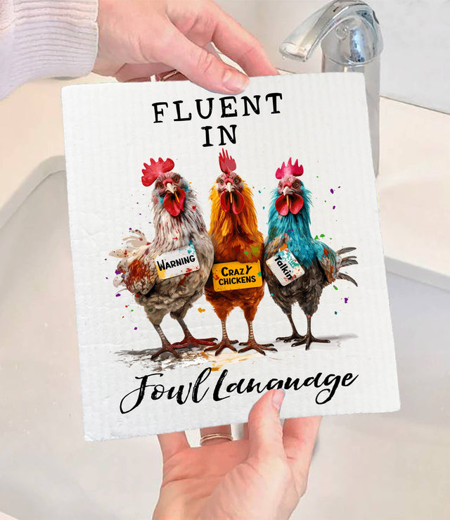 Someone holds the Dish Cloth: Fluent in Fowl Language Funny Saying SWEDISH DISH CLOTH, featuring three illustrated chickens with signs—Warning, Crazy Chickens, Fowl Mouth—and the phrase Fluent in Fowl Language. Eco-friendly and humorous!.