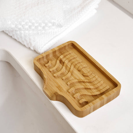 Bamboo soap lift with wavy grooves on a white bathroom countertop beside folded white towels.