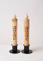 The Home Sweet Home Sunflower LED Timer Taper Candle: Top Dusted features two battery-operated tapers on black stands, each with a sunflower and phrase design, creating a cozy, charming ambiance against a white background.
