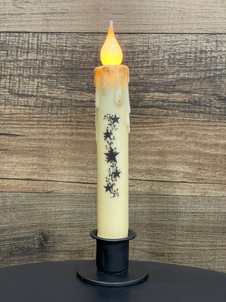 A battery-operated candle featuring a melted wax look and star decorations is displayed in a Round Wrought Iron Taper Candle Holder, set against a wooden background.