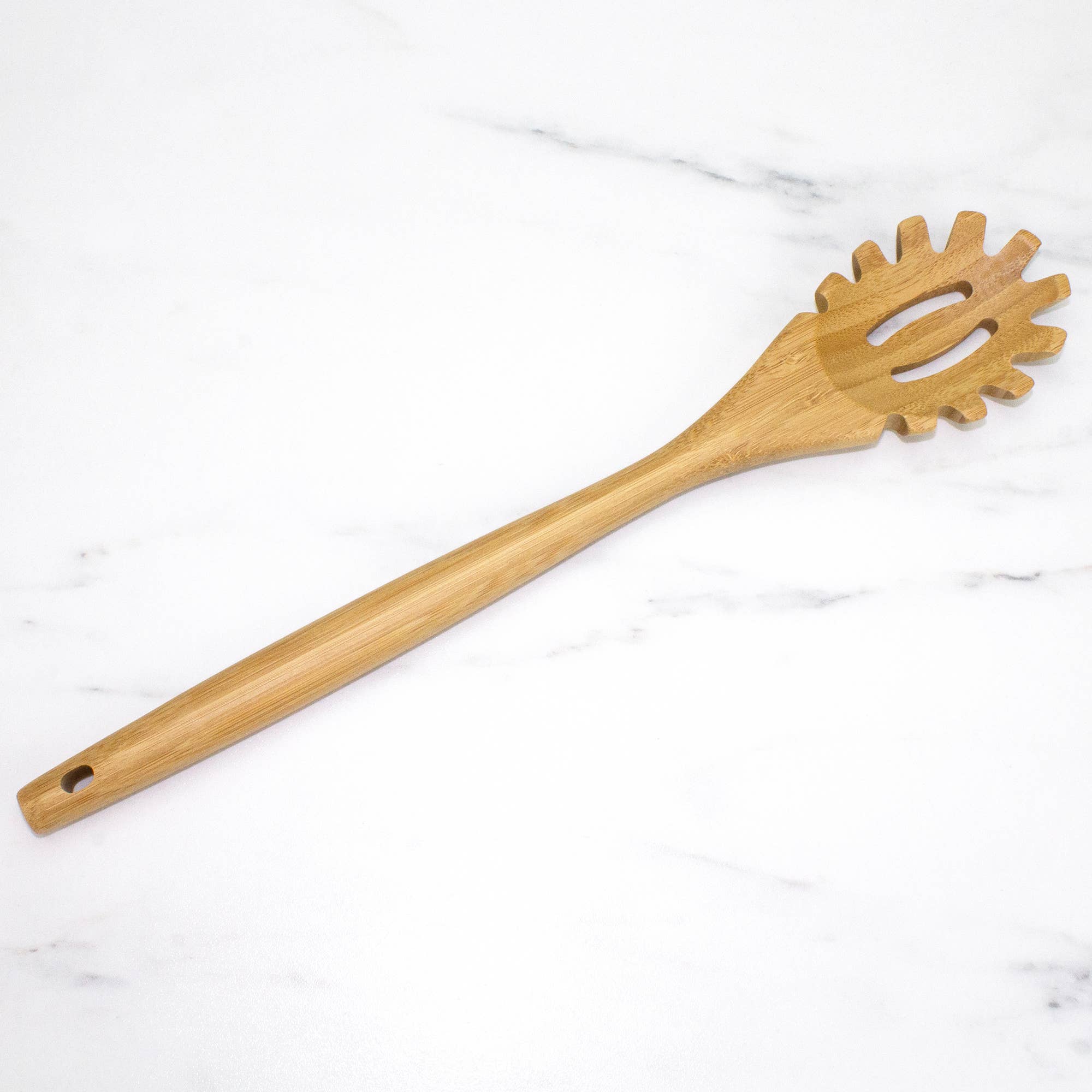 The Utensil: 14" Spaghetti Server Lambootensil Bamboo, made from natural bamboo, showcases a long handle and pronged end as it gracefully rests on a white marble surface.