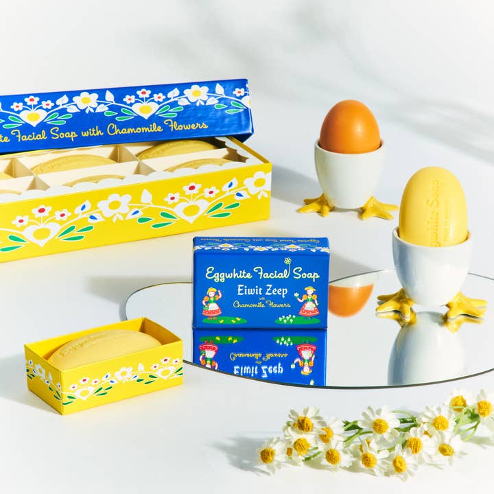 Boxes and bars of Soap: Eggwhite & Chamomile Facial Soap – 2.25 oz, a gentle daily cleanser, are displayed with a mirror, egg cups, and fresh chamomile flowers.