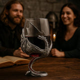A smiling man and woman sit at a table with an open book and the Wine Glass: Medieval Dragon Viking Goblet Mug – Fantasy-Inspired Drinkware (9oz), featuring a dragon-shaped metal holder.