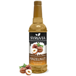 A bottle of Syruvia Hazelnut Coffee Syrup with Pure Cane Sugar, featuring hazelnut images and loose hazelnuts—perfect as a gluten-free coffee syrup.