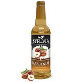 A bottle of Syruvia Hazelnut Coffee Syrup with Pure Cane Sugar, featuring hazelnut images and loose hazelnuts—perfect as a gluten-free coffee syrup.