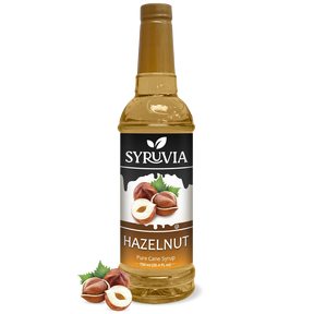 A bottle of Syruvia Hazelnut Coffee Syrup with Pure Cane Sugar, featuring hazelnut images and loose hazelnuts—perfect as a gluten-free coffee syrup.