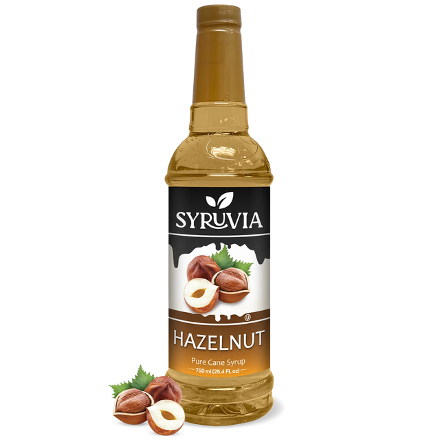 A bottle of Syruvia Hazelnut Coffee Syrup with Pure Cane Sugar, featuring hazelnut images and loose hazelnuts—perfect as a gluten-free coffee syrup.