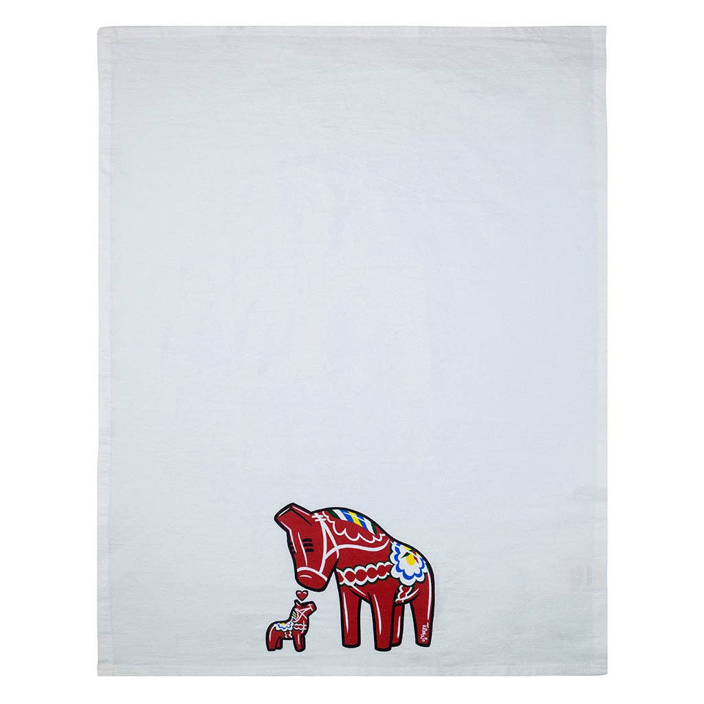 The Tea Towel - Dala Horse "Jumbo" by Adam Turman is a white cloth with a red Dala Horse and floral designs, ideal for Scandinavian kitchen decor. A small red horse with a person stands near the bottom corner.