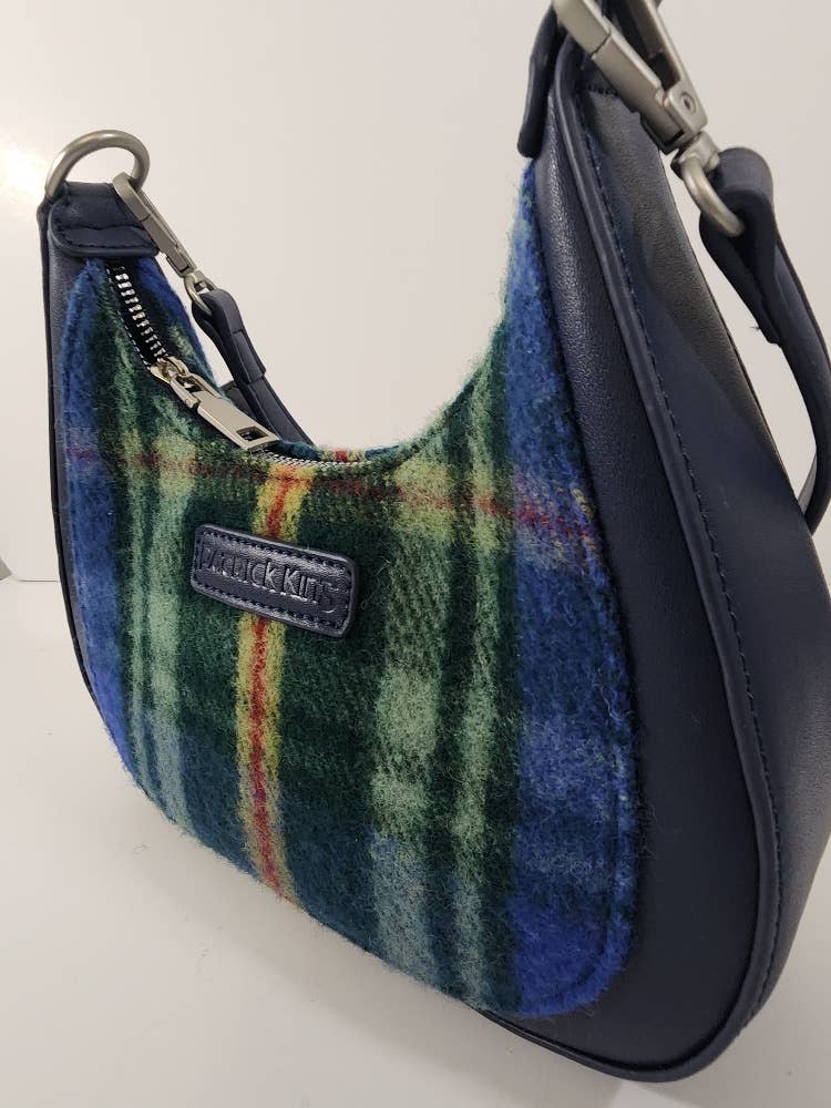 The Tartan Merino Wool Bag - Nova Scotia is a small handbag with dark blue leather sides and strap, featuring a green, blue, and red Nova Scotia tartan fabric panel and a visible zipper.