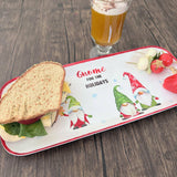 Melamine tray on a wooden table, featuring gnome illustrations and “Gnome for the Holidays” text, with a sandwich, vegetables, and a drink placed on top.