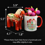 A hand-carved Färnäshästen Red Swedish Dala Horse by Nils Olsson (14 cm/5.5 in) stands beside a white mug filled with pink felt balls, with its dimensions clearly labeled by arrows.
