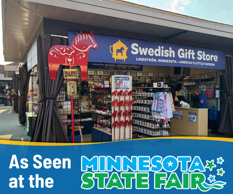 Display booth with Dala horses, souvenirs, a Minnesota State Fair banner, and a red metal Dala horse garden stake among Scandinavian-themed outdoor accents.