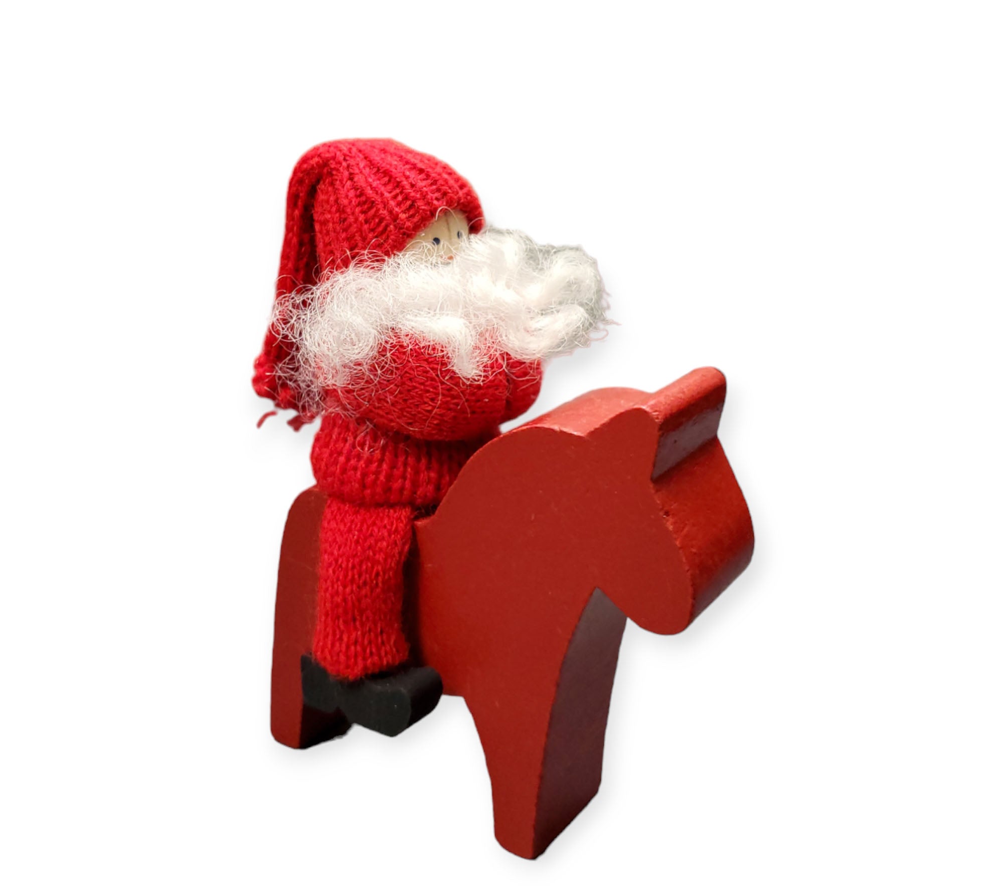 The Handcrafted Swedish Tomte Boy or Girl figurine, shown on a vibrant red wooden Dala horse, features a red knitted outfit and white beard, adding Nordic charm to any white background setting.