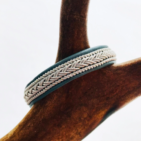 Bracelet: Lapland Sami with Reindeer Hyde, Pewter & Silver Bracelet #2 - Tennis - Black, handcrafted in Sweden with intricate braiding and dark edges, shown on a brown wooden branch.