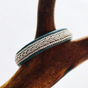 Bracelet: Lapland Sami with Reindeer Hyde, Pewter & Silver Bracelet #2 - Tennis - Black, handcrafted in Sweden with intricate braiding and dark edges, shown on a brown wooden branch.