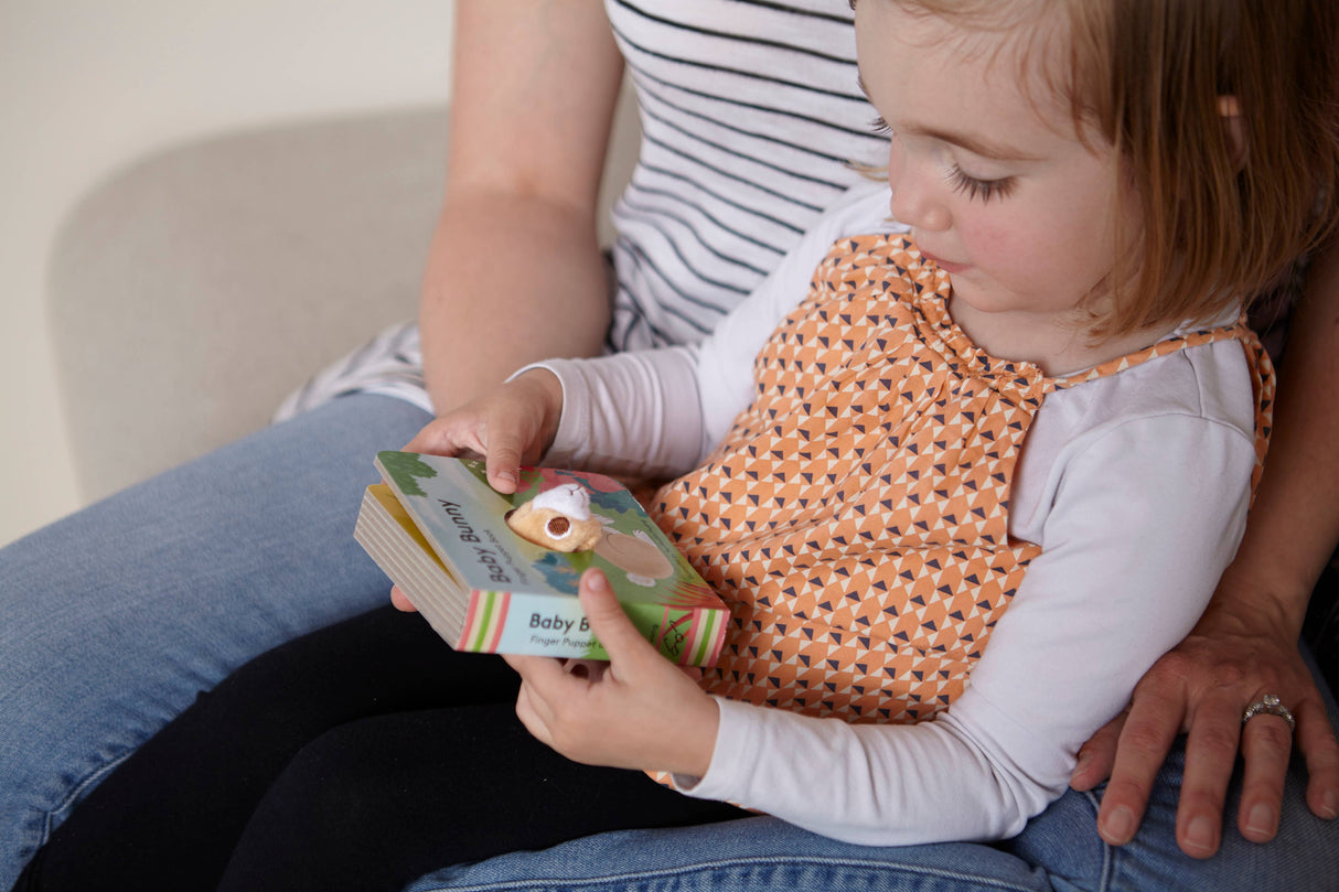 A young child sits on an adult's lap, exploring the Book: Baby Bunny Finger Puppet Book, which features a playful animal illustration on the cover.