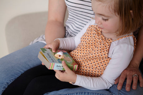 A young child sits on an adult's lap, exploring the Book: Baby Bunny Finger Puppet Book, which features a playful animal illustration on the cover.