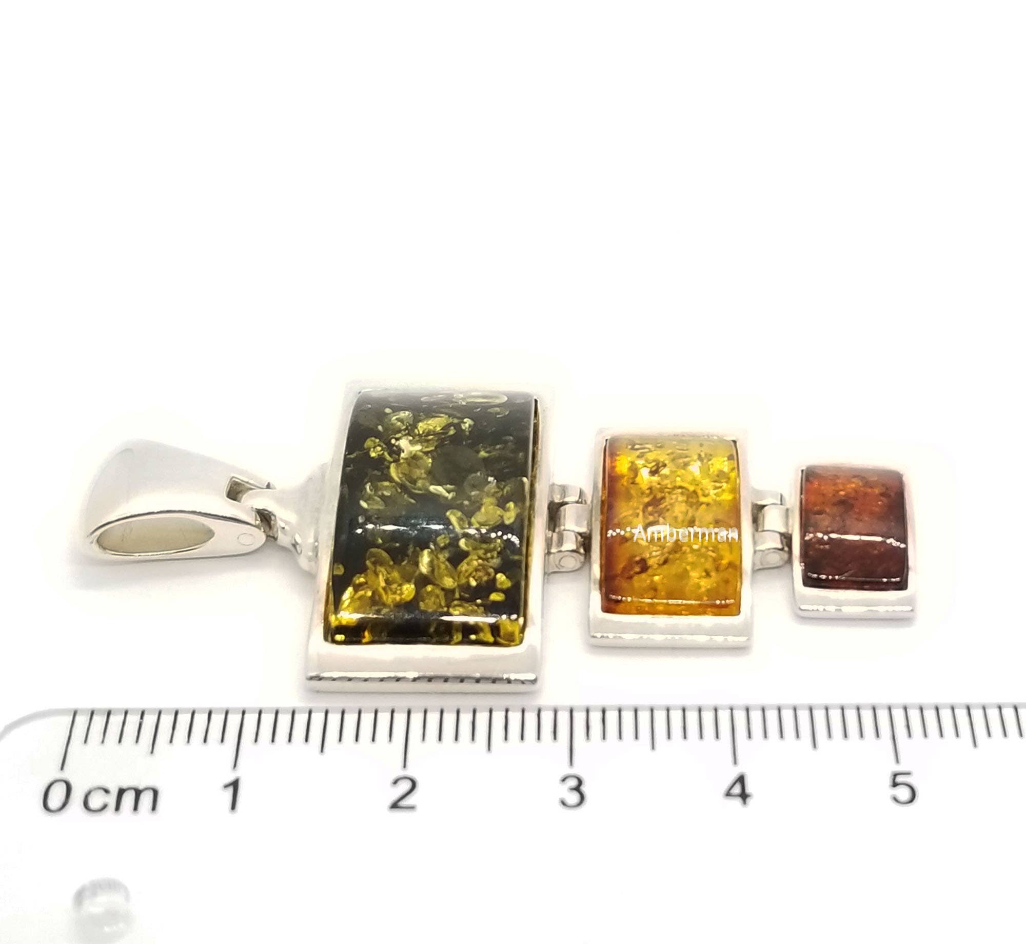 Three rectangular pendants from the Multi-Color 3 Amber Stones Set in Sterling Silver are aligned next to a centimeter ruler, crafted with genuine Baltic Amber of varying colors and sizes.