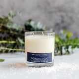 An 8oz Nordic Fog Candle sits on a white surface with scattered salt and green foliage, evoking the fresh scent of eucalyptus mint in the background.