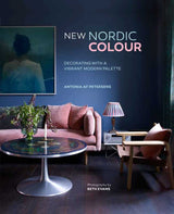 A modern living room with a pink sofa, round coffee table, and armchair exudes Scandinavian style, featuring the Book: New Nordic Colour by Antonia af Petersens on display.