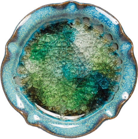 Handmade in the USA, this 5.75" diameter pottery candle holder features a blue rim and a glossy, textured interior with green, blue, and clear recycled glass fused together. Perfect for pillar & ball candles.