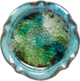 Handmade in the USA, this 5.75" diameter pottery candle holder features a blue rim and a glossy, textured interior with green, blue, and clear recycled glass fused together. Perfect for pillar & ball candles.
