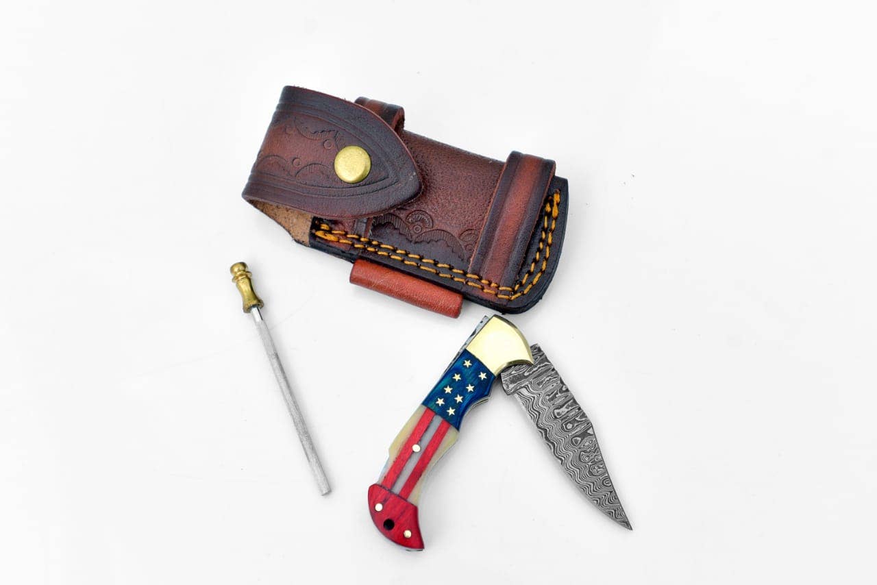 The Damascus Steel Pocket Knife Titan Patriot features an American flag handle, patterned blade, small sharpening rod, and a brown leather snap-closure sheath.