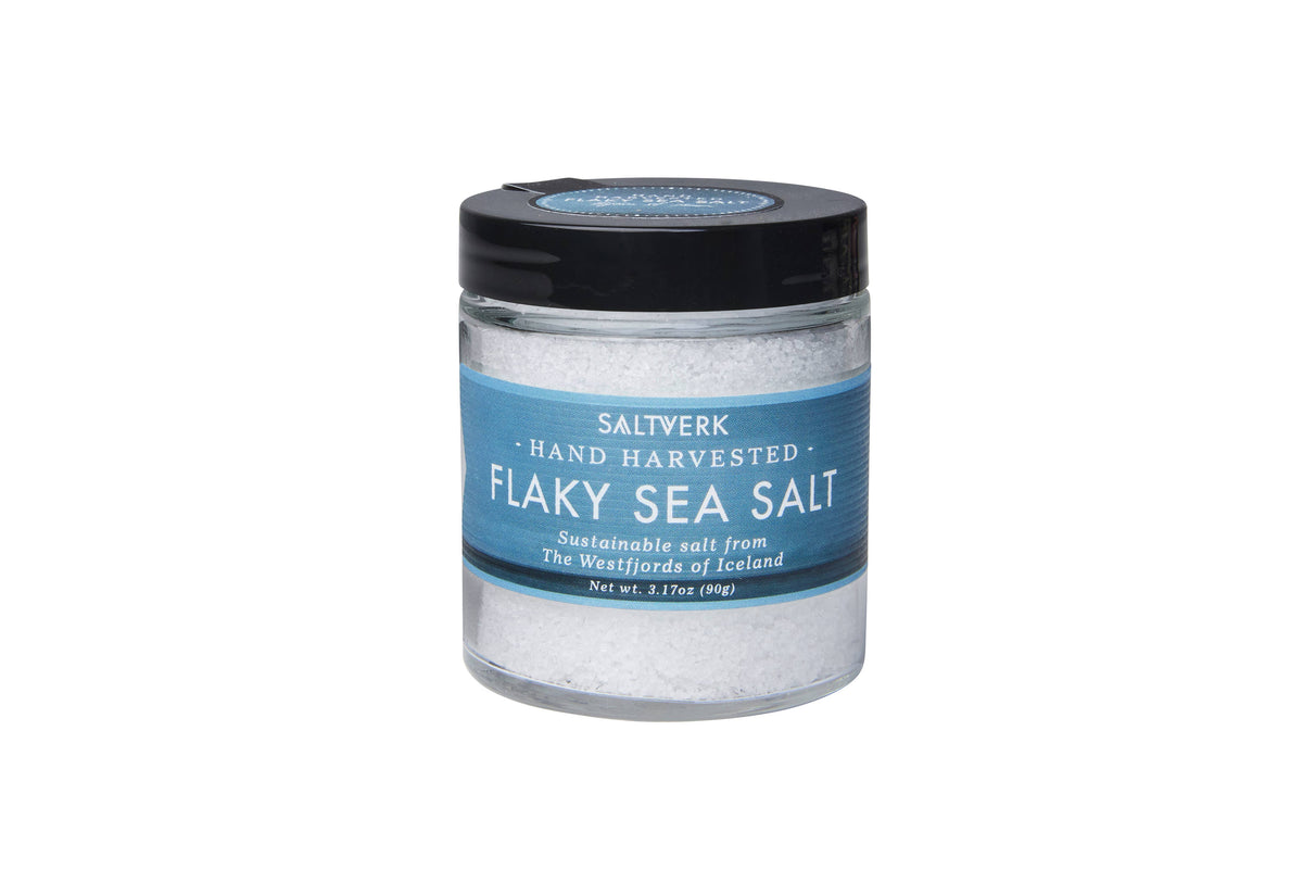 A clear jar with a black lid from the SALTVERK Gift Set contains hand-harvested pure Icelandic sea salt flakes, available in Flaky Sea Salt, Lava Salt, Birch Smoked Salt, and Arctic Thyme Salt varieties.