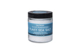 A clear jar with a black lid from the SALTVERK Gift Set contains hand-harvested pure Icelandic sea salt flakes, available in Flaky Sea Salt, Lava Salt, Birch Smoked Salt, and Arctic Thyme Salt varieties.