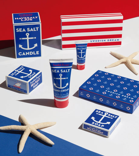 A selection of Swedish Dream Sea Salt items, featuring vegan and cruelty-free products like the Sea Salt Soap, along with hand cream and a candle, beautifully arranged with starfish on a red, white, and blue backdrop.