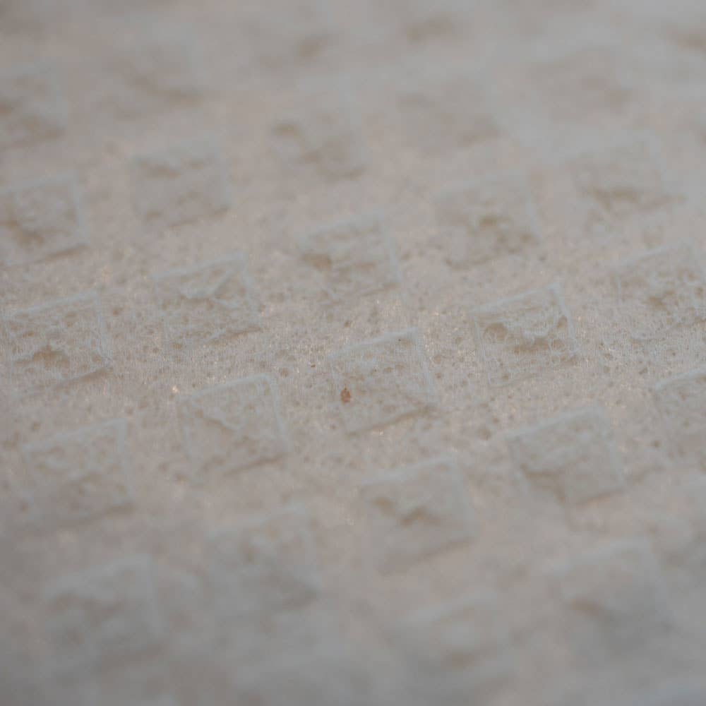 Close-up of a textured surface featuring a grid pattern of raised square shapes, reminiscent of the eco-friendly design found in the Home Sweet Home Swedish Dishcloth.