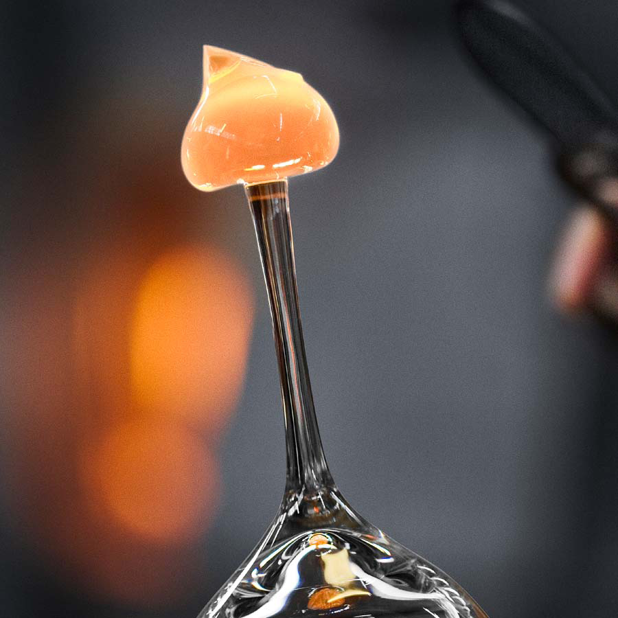 A close-up of a glowing molten glass piece on a rod evokes the elegance of Erika Lagerbielkes design style for the Orrefors Difference Mature Glass 22oz (2-Pack), set against a blurred background.