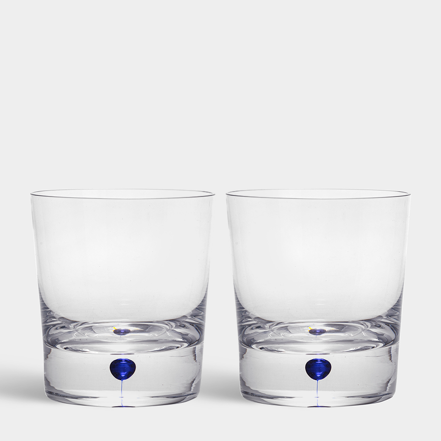 The Orrefors Intermezzo Blue Double Old Fashioned Whiskey set, designed by Erika Lagerbielke, features two 11oz clear glass tumblers with a subtle blue accent at the base, blending simplicity and artistic flair on a plain backdrop.