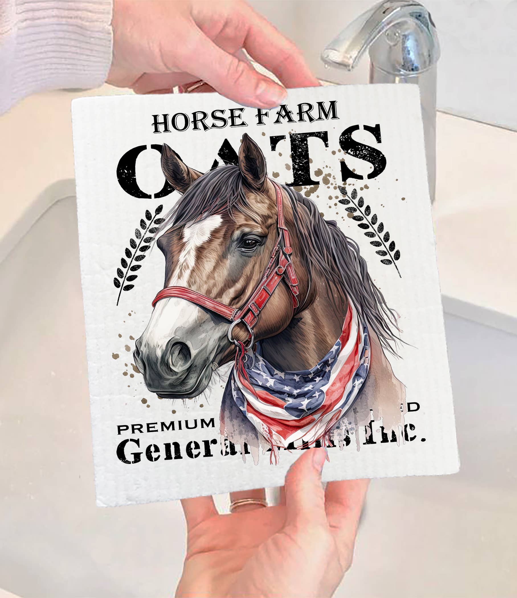 A person is holding a Horse Farm Oats Farmhouse SWEDISH DISH CLOTH featuring a horse illustration with an American flag halter. The text on the cloth reads "Horse Farm Oats, Premium Food, General Purpose." This eco-friendly product brings both charm and sustainability to your kitchen essentials.