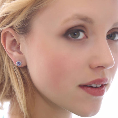 A woman with light skin and blonde hair wears small, round Ruby Red Swarovski Crystal Handmade Silver Solitaire Stud Earrings and subtle makeup, shown in a close-up portrait from the shoulders up.
