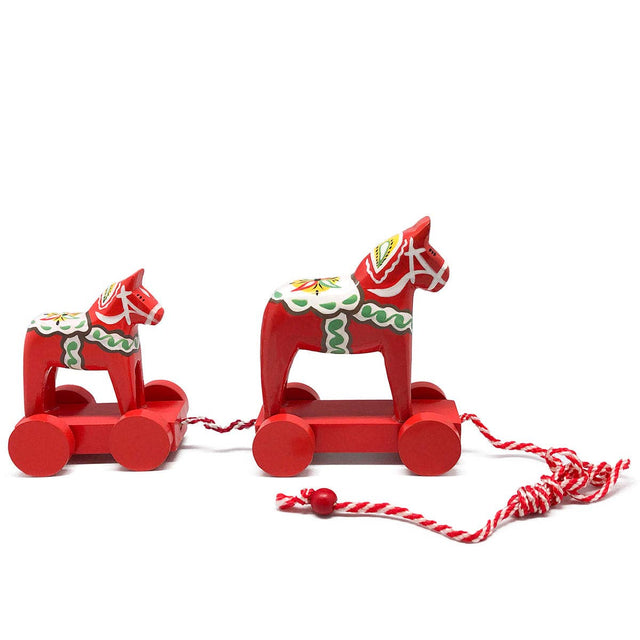 A red wooden pull toy featuring two Swedish Dala horses (5 inches and 4 inches tall) on wheels with a 26-inch red and white pull string, decorated with traditional Nordic folk art motifs.
