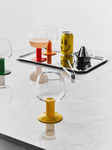 Fars Glas wine glasses with colored stems on a marble surface next to a tray with a drink can, citrus juicer, and tongs.