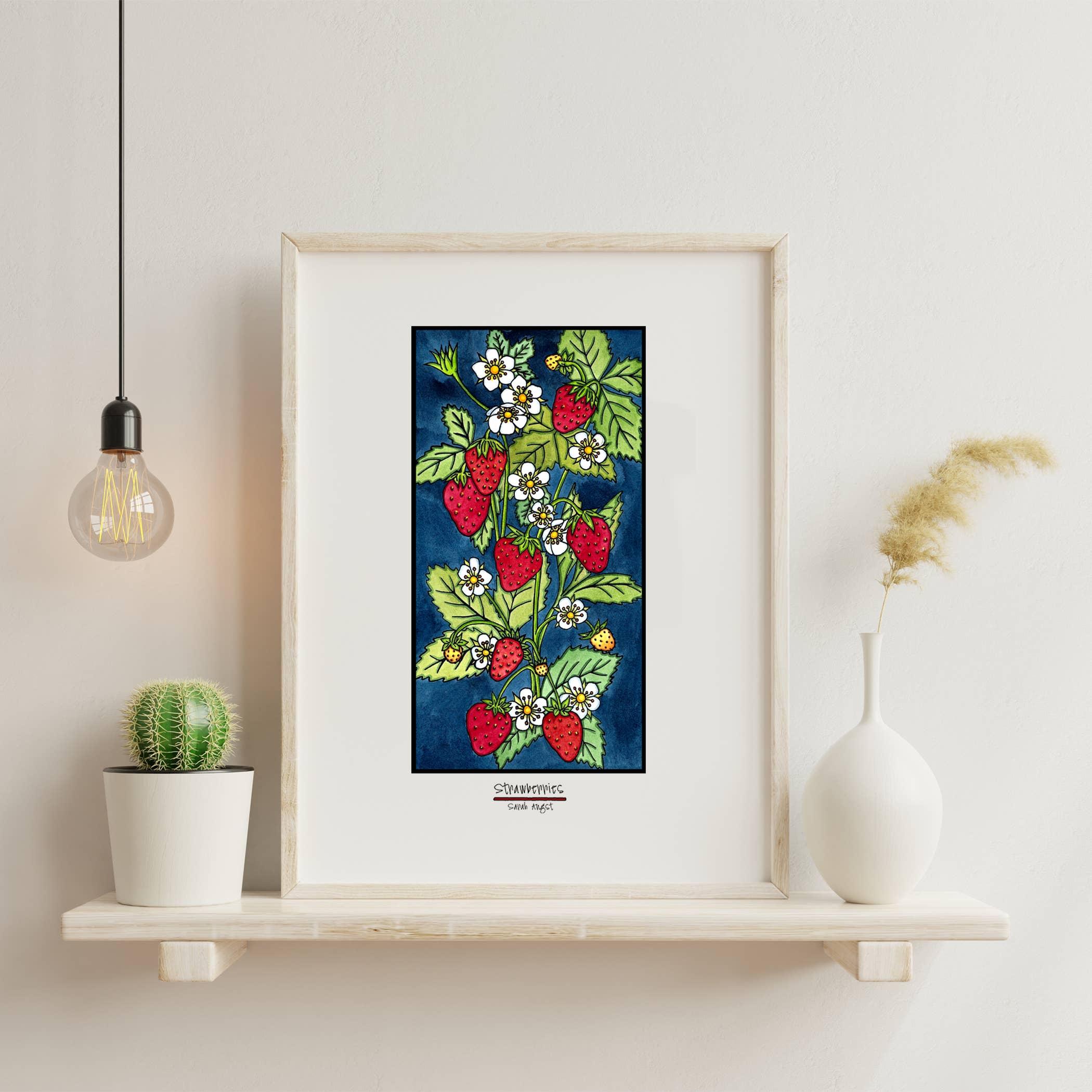 The "Artwork: Strawberries: Black Frame 11\"x14\"" features a lively depiction of a strawberry plant adorned with ripe berries and delicate flowers. Elegantly placed on a shelf beside a cactus, vase, and trendy hanging light bulb, it adds character to any room.