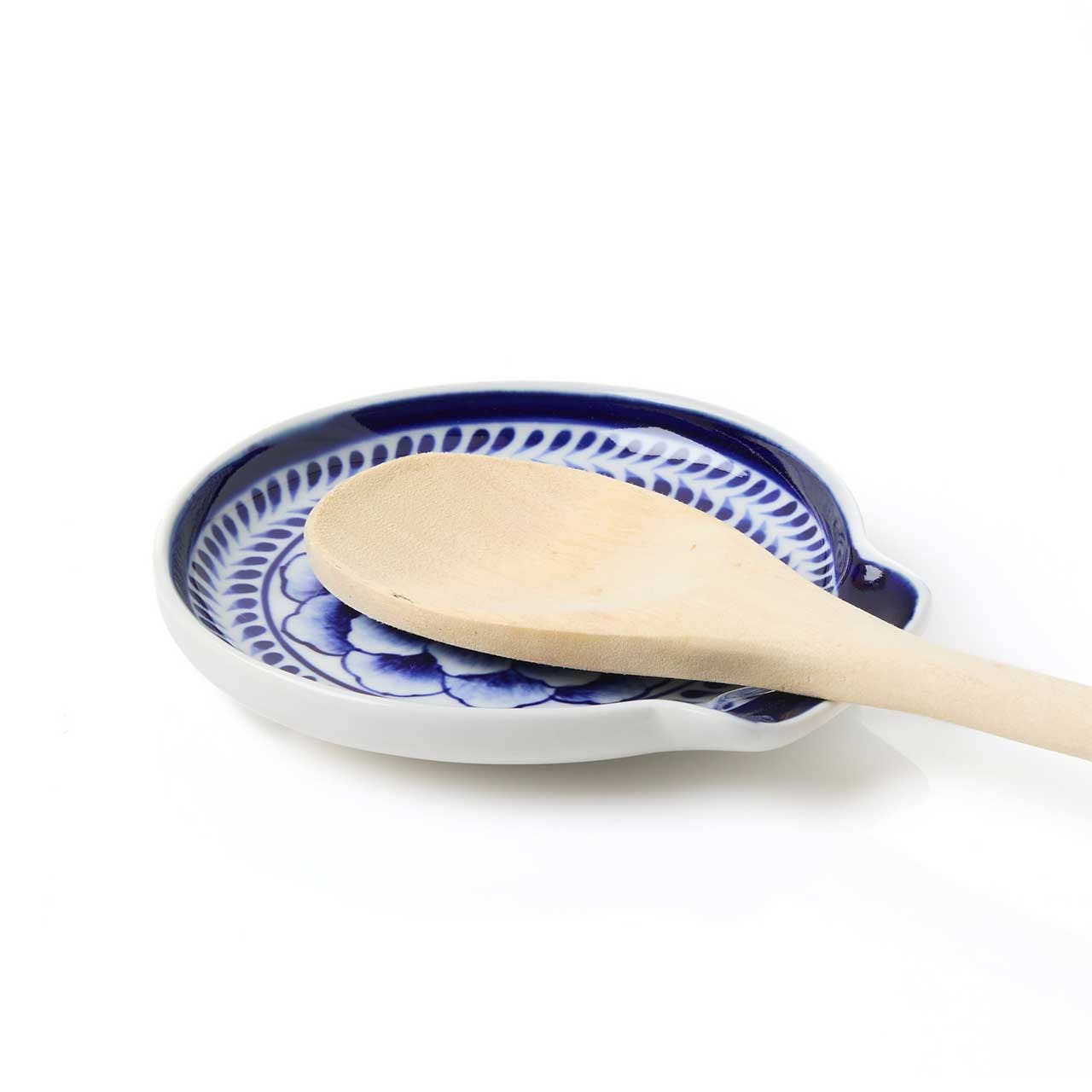 A wooden spoon sits on the Indigo Bloom Spoon Rest, a hand-painted Bat Trang ceramic piece with blue and white patterns, set against a white background.