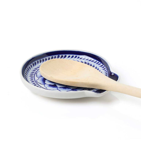 A wooden spoon sits on the Indigo Bloom Spoon Rest, a hand-painted Bat Trang ceramic piece with blue and white patterns, set against a white background.